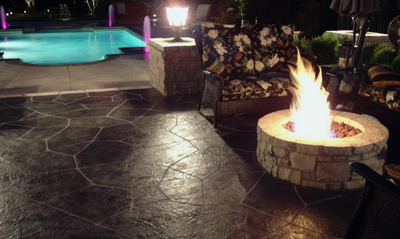Textured pool deck next to a dark stained and stamped concrete patio and built in fire pit.